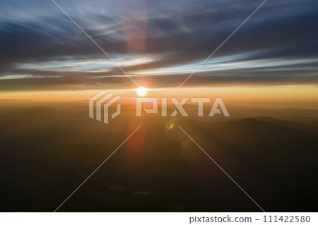 Aerial view of dark mountain hills with bright sunrays of setting sun at sunset. Hazy peaks and misty valleys in evening 111422580