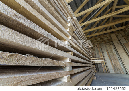 Neatly piled long stack of wooden boards inside attic room under construction. Neatly piled long stack of wooden boards inside attic room under construction. 111422662