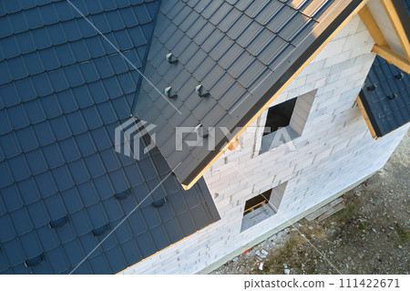 Aerial view of unfinished house with aerated lightweight concrete walls and wooden roof frame covered with metallic tiles under construction. Aerial view of unfinished house with aerated lightweight concrete walls and wooden roof frame covered with metallic tiles under construction. 111422671