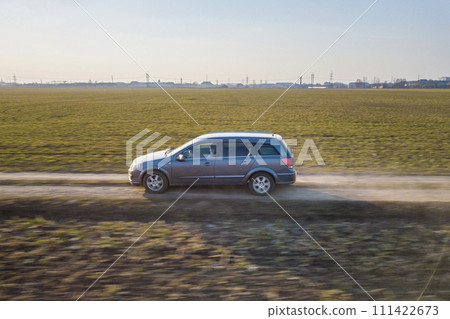 Aerial view of car driving by straight ground road through green fields on sunny blue sky copy space background. Drone photography. Aerial view of car driving by straight ground road through green fields on sunny blue sky copy space background. Drone photography. 111422673