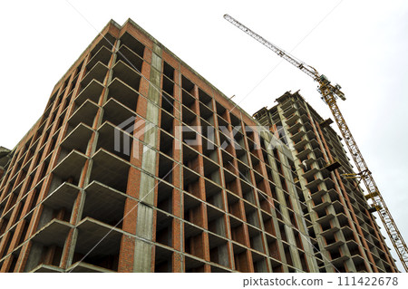 Ground view of a new modern residential house building under construction. Real estate development concept. Multi story home from bricks and concrete. Construction site tower crane at work. 111422678