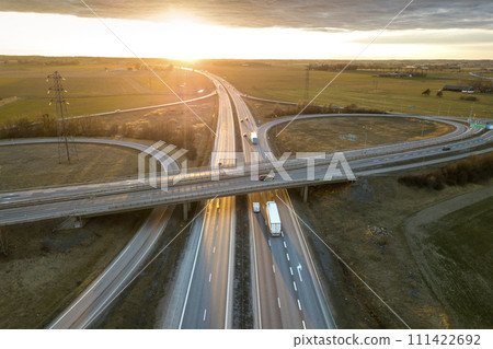 Aerial view of modern highway road intersection at dawn on rural landscape and raising sun background. Drone photography. 111422692