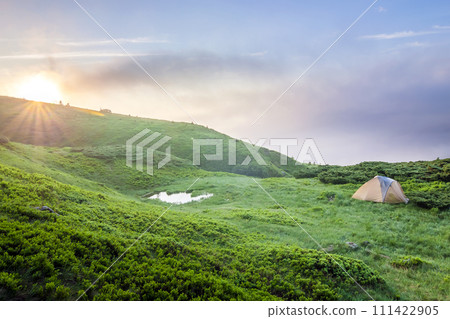 Sunrise in mountains with a tourist tent and a little lake in view 111422905