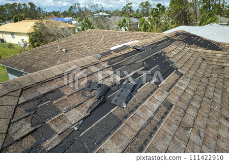 Wind damaged house roof with missing asphalt shingles after hurricane Idalia in Florida. Repair of home rooftop concept Wind damaged house roof with missing asphalt shingles after hurricane Idalia in Florida. Repair of home rooftop concept 111422910