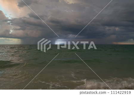 Dark ominous thunderstorm clouds forming on overcast sky during heavy rainfall season over ocean surface at sunset 111422919