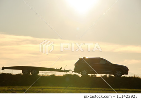 Tow truck vehicle with car transporting carrier trailer driving on highway in evening Tow truck vehicle with car transporting carrier trailer driving on highway in evening 111422925