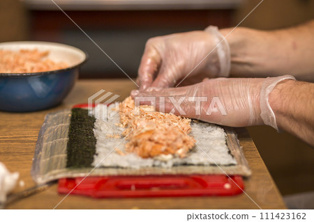 Process of making sushi and rolls. Close-up of man chef hands preparing traditional Japanese food at home or in restaurant on kitchen table. 111423162