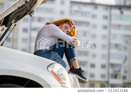 Young stressed woman driver near broken car with popped hood waiting for assistance. 111423166