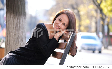 Young happy woman sitting relaxed on street bench on warm autunm day. Wellness and resting from everyday rush concept 111423167