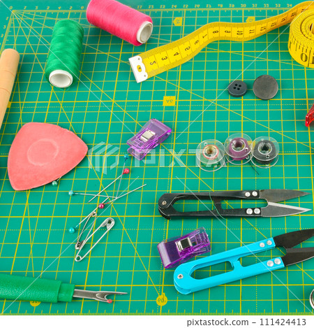 A set of sewing supplies laid out on a patchwork mat. 111424413