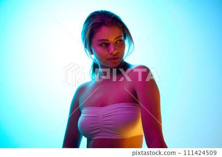 Elegant beautiful young girl with ponytail, wearing white op, standing against gradient studio background in neon light. Beauty makeup campaign 111424509