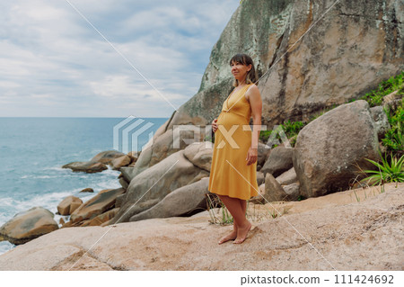 Pregnant woman in yellow dress posing at summer ocean coastline 111424692