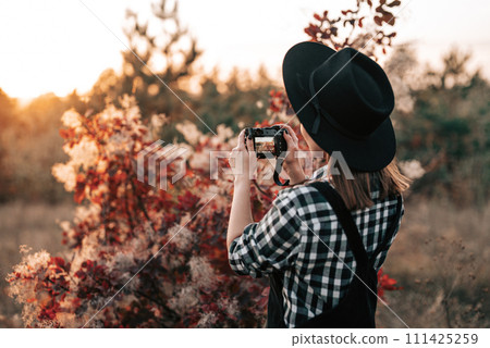 Young pretty woman takes pictures with DSLR camera outdoors on autumn background 111425259