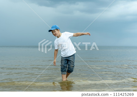 A boy in a white shirt and blue hat is standing in the water A boy in a white shirt and blue hat is standing in the water 111425269