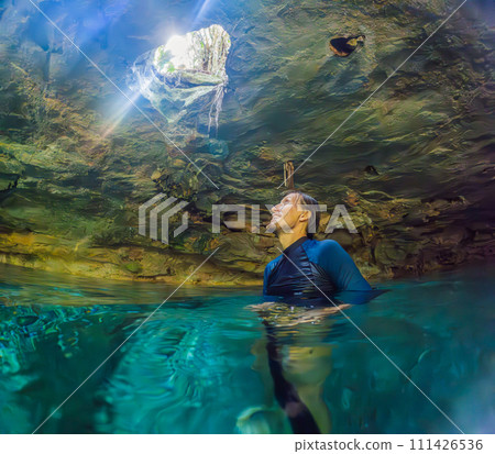Man immersed in the enchanting beauty of a Mexican cenote, surrounded by crystal-clear waters and captivating natural formations 111426536