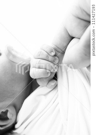 Close-up of baby's small hand, head, ear and palm of mother. Macro. Black and white Photo of Newborn baby after birth tightly holding parents finger. Family and home concept. Healthcare, paediatrics Close-up of baby's small hand, head, ear and palm of mother. Macro. Black and white Photo of Newborn baby after birth tightly holding parents finger. Family and home concept. Healthcare, paediatrics 111427193