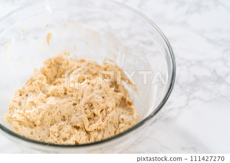 Mixing wet and dry ingredients with a hand whisk in a glass mixing bowl to bake lemon poppy seed muffins. 111427270