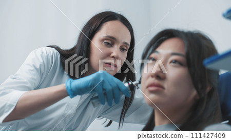 Female doctor otolaryngologist checks ears of patient Female doctor otolaryngologist checks ears of patient 111427409