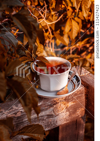 White porcelain tea cup on the wooden balcony yellow wild grapes background. Warm healthy herbal drink.Weekend breakfast 111427423