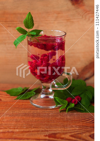 Summer raspberry cold tea in a glass on wooden background. Healthy fruit cocktail. Tasty red juice fresh green leaves. 111427446