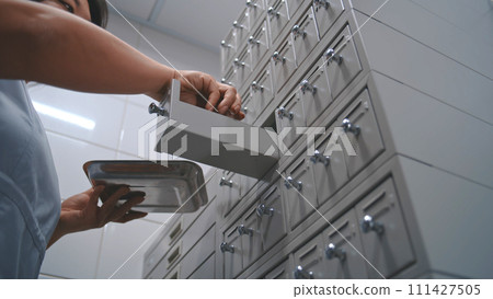 Asian nurse puts samples with blood tests in medical storage cabinet 111427505