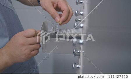 Male nurse puts samples with blood tests in medical storage cabinet Male nurse puts samples with blood tests in medical storage cabinet 111427530