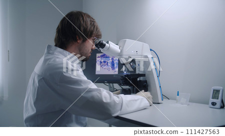 Male scientist looks under microscope in modern laboratory Male scientist looks under microscope in modern laboratory 111427563