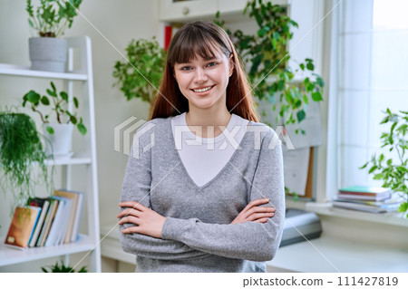 Portrait of smiling female teenager looking at camera with crossed arms in home 111427819