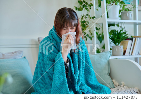 Young sick woman sitting under warm blanket sneezing coughing in handkerchief 111427875