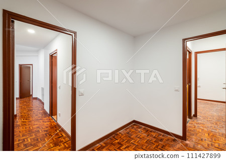 An apartment with corridor leading to empty rooms with wooden doors  111427899