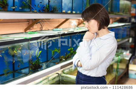 Pensive woman searching aquarium fish Pensive woman searching aquarium fish 111428686