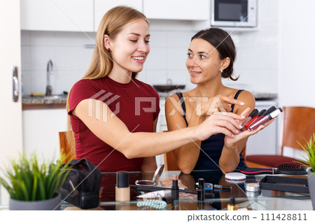 Two smiling young female friends looking cosmetics before make-up at table Two smiling young female friends looking cosmetics before make-up at table 111428811