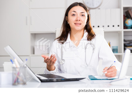 Girl doctor in uniform is writing papers behind laptop 111429624