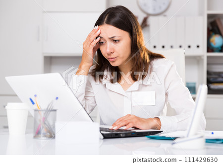 Upset woman working with laptop and papers at the office Upset woman working with laptop and papers at the office 111429630