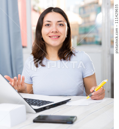 Girl student working with laptop and pen at table in home Girl student working with laptop and pen at table in home 111429635