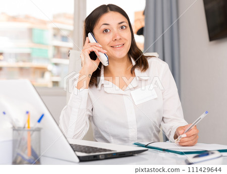 Young woman using laptop and talking by phone at the office Young woman using laptop and talking by phone at the office 111429644