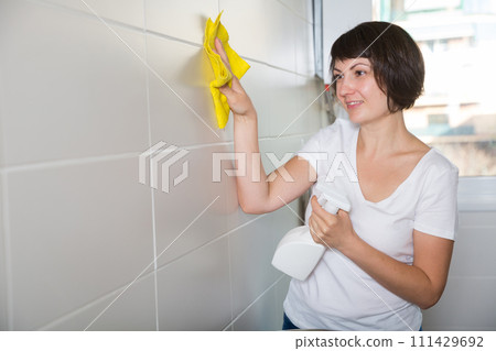 Woman with detergent cleaning tiled wall Woman with detergent cleaning tiled wall 111429692