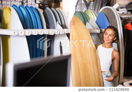 Positive female holding surfboard in the sports store 111429699