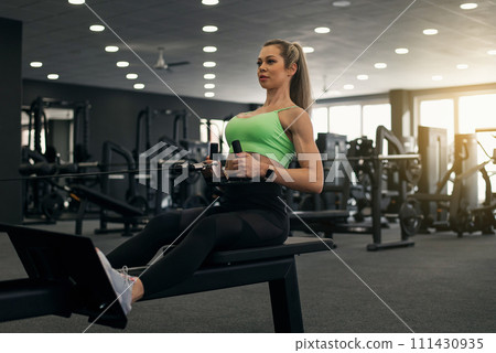 Attractive sportswoman exercising on seated low cable row machine. Sporty and healthy lifestyle motivation. Attractive sportswoman exercising on seated low cable row machine. Sporty and healthy lifestyle motivation. 111430935