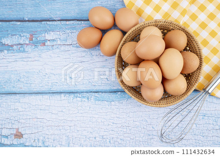 Overhead view of brown chicken eggs in weave basket and a whisk on wooden background. Overhead view of brown chicken eggs in weave basket and a whisk on wooden background. 111432634