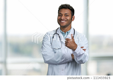 Handsome young doctor with stethoscope giving thumb up to camera. Smiling male doctor looking at camera. Handsome young doctor with stethoscope giving thumb up to camera. Smiling male doctor looking at camera. 111433923