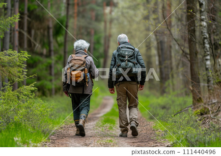 An elderly couple walks with backpacks along a forest path An elderly couple walks with backpacks along a forest path 111440496