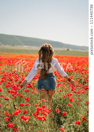 Woman poppies field. Back view of a happy woman with long hair in a poppy field and enjoying the beauty of nature in a warm summer day. 111440786