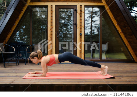 Woman does plank exercise on the porch of a-frame cabin 111441062