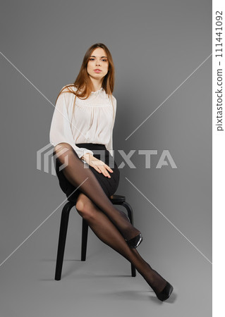 Stylish young woman with long legs in black tights sits on a chair Stylish young woman with long legs in black tights sits on a chair 111441092