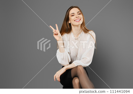 Satisfied woman sitting on a chair raising two fingers showing a symbol of victory 111441094