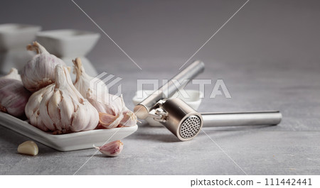 Garlic and garlic press on a grey table. Garlic and garlic press on a grey table. 111442441