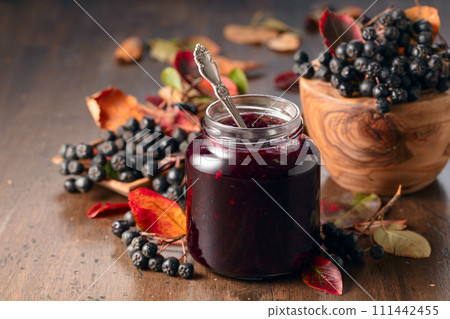 Chokeberry jam and fresh berries on an old wooden table. Chokeberry jam and fresh berries on an old wooden table. 111442455