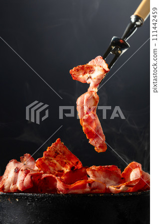Fried steaming bacon slices on a black background. 111442459