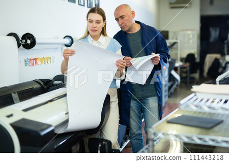 Service engineer and office worker checking printed document together against color chart closeup 111443218